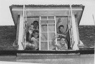 A group of boys wave from one of the windows in their accommodation in the Stables complex. Left from top: Arnold, Richard and Juek. Behind the centre glass: Stachek.  Right from top: Leonard and Niko. | From the earlypestalozzichildren.org.uk website