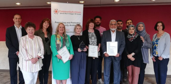 The award winners at the CAHG 2019 Conference. A line of people stand in front of a banner for the conference.